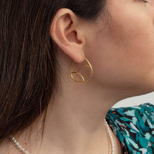 Close view of a geometric teardrop hoop earring worn on the lobe with a green print top