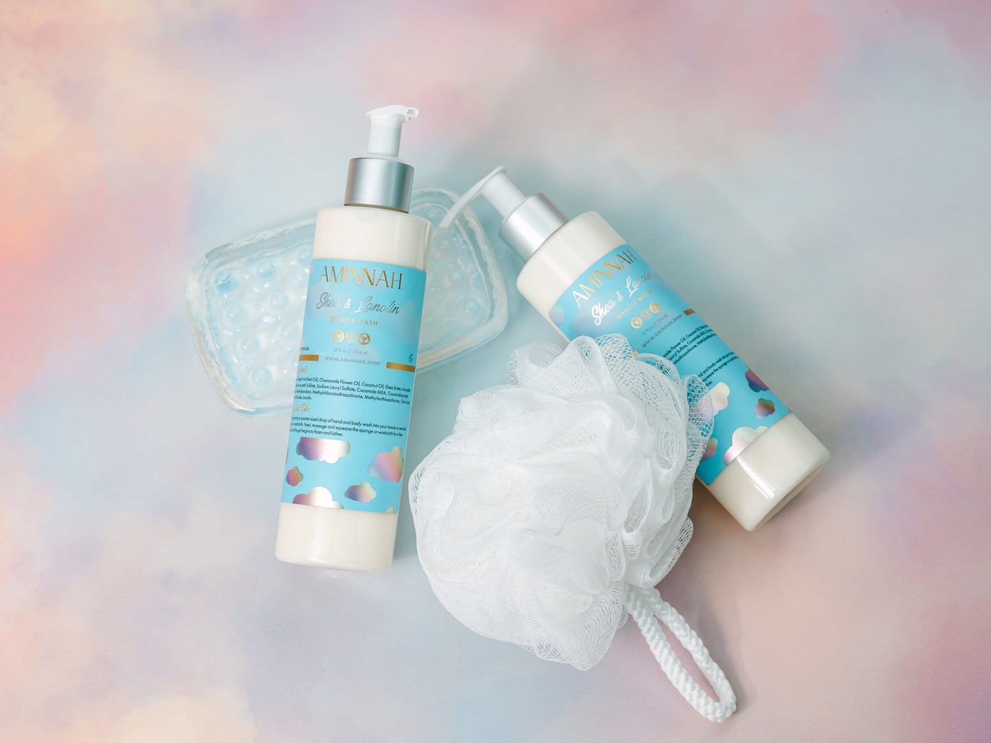 Cleanser bottles beside a white mesh bath puff on pastel.