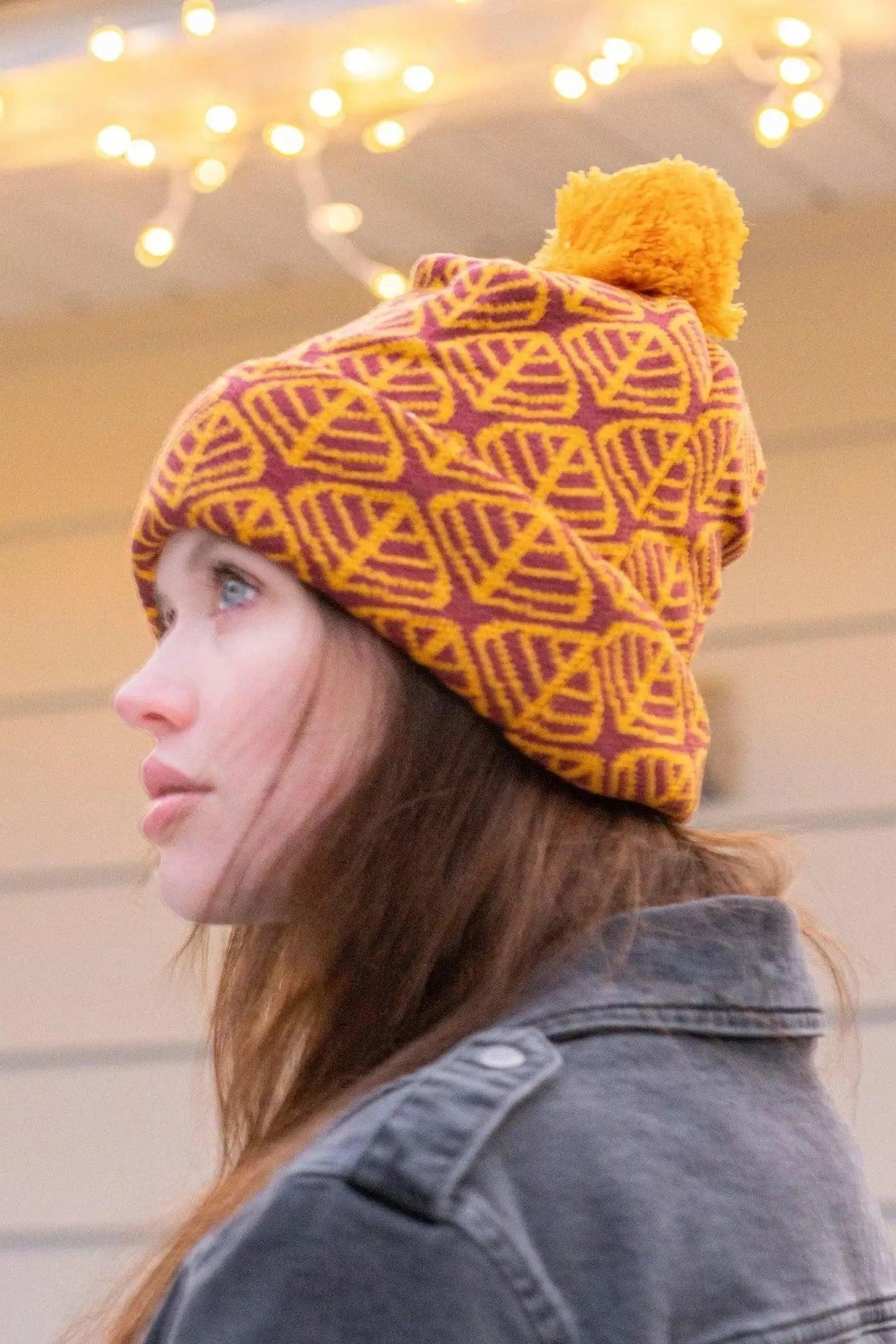 Side view of the burgundy leaf pattern beanie and its mustard pom pom on a model