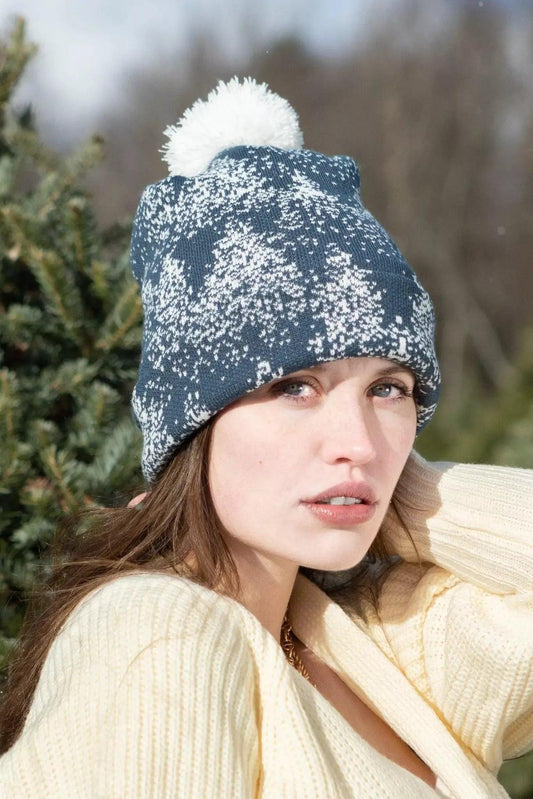 Model in the spruce pattern pom pom beanie, standing among evergreen trees