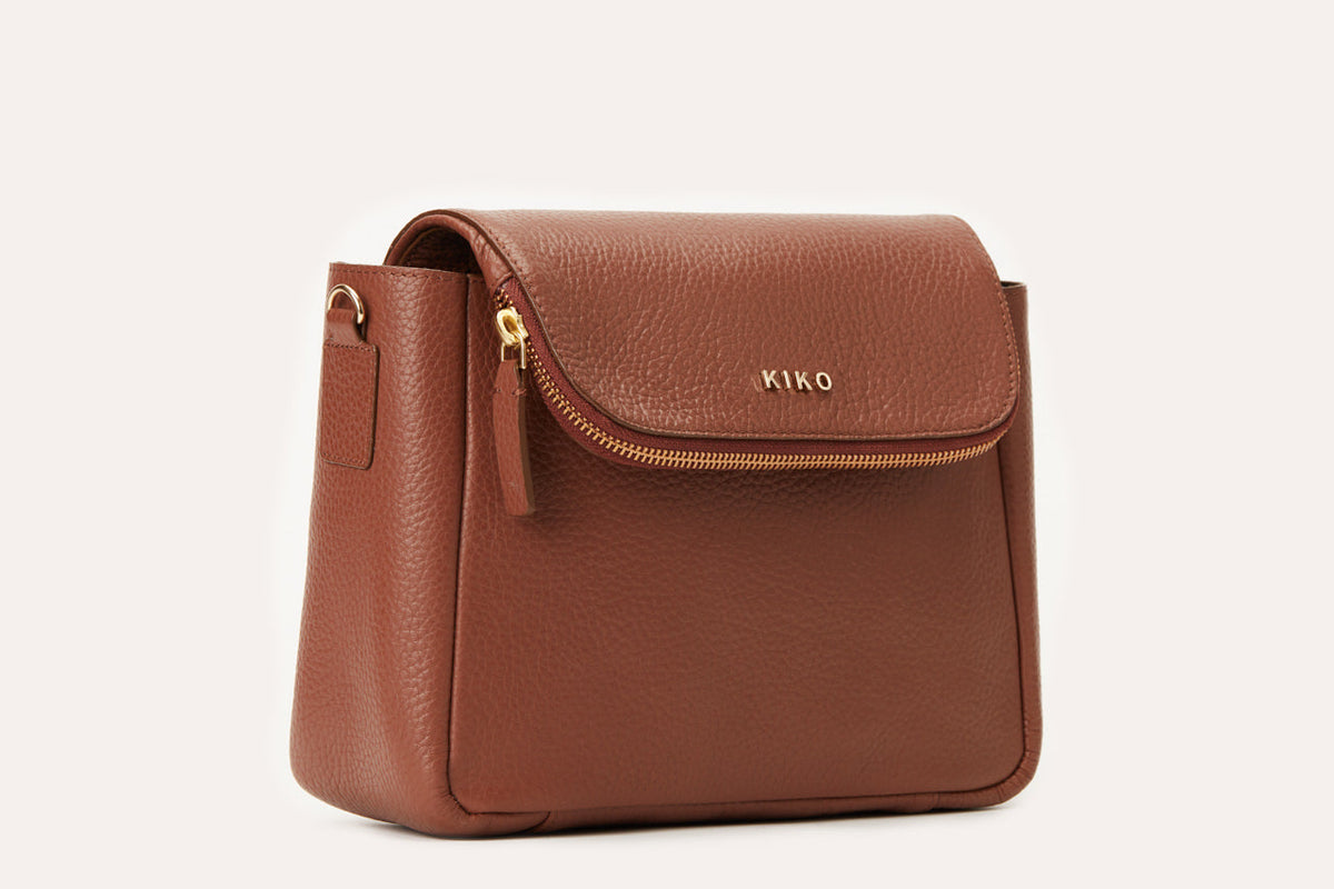 Dark brown pebbled leather flap crossbody bag with a gold-tone zip along the flap, three-quarter view