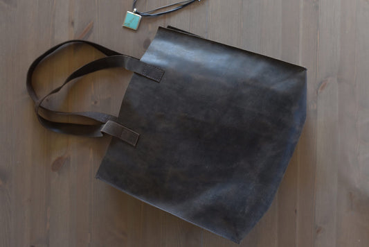 Marbled brown leather tote lying on a wood floor beside a turquoise pendant, handles fanned out