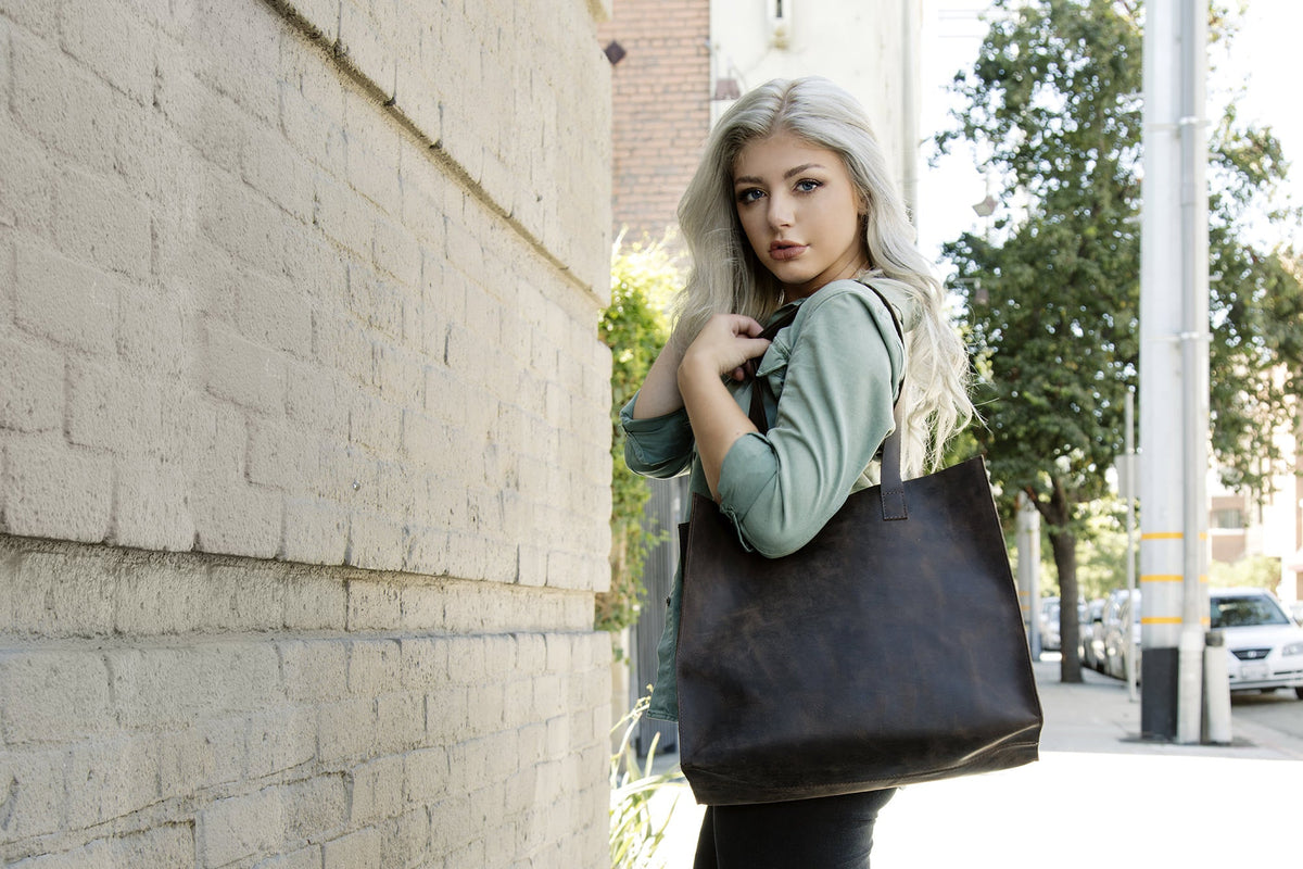 Woman by a brick wall carrying the marbled brown leather tote on her shoulder