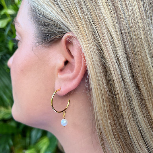 Woman wearing a gold plated hoop earring with a freshwater pearl drop, seen in profile outdoors