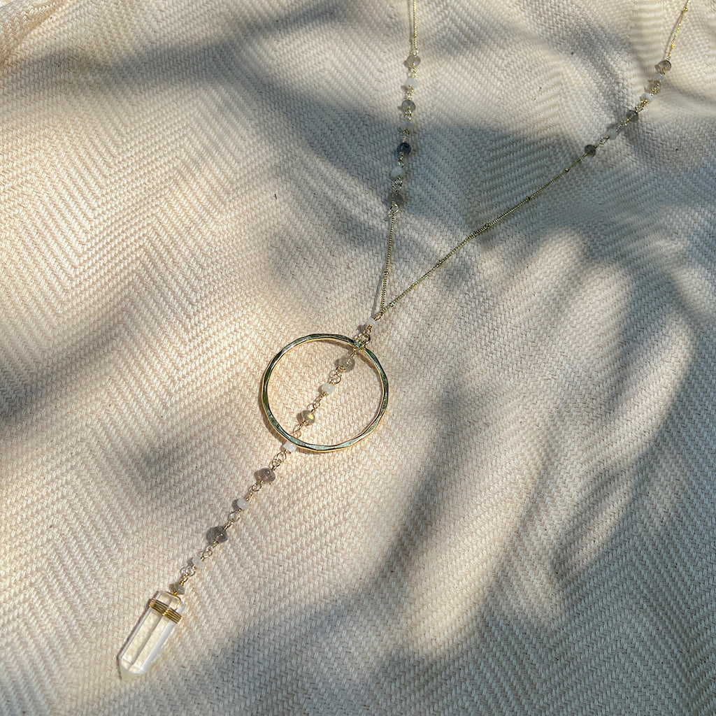 Clear quartz Y necklace on cream herringbone fabric in dappled light