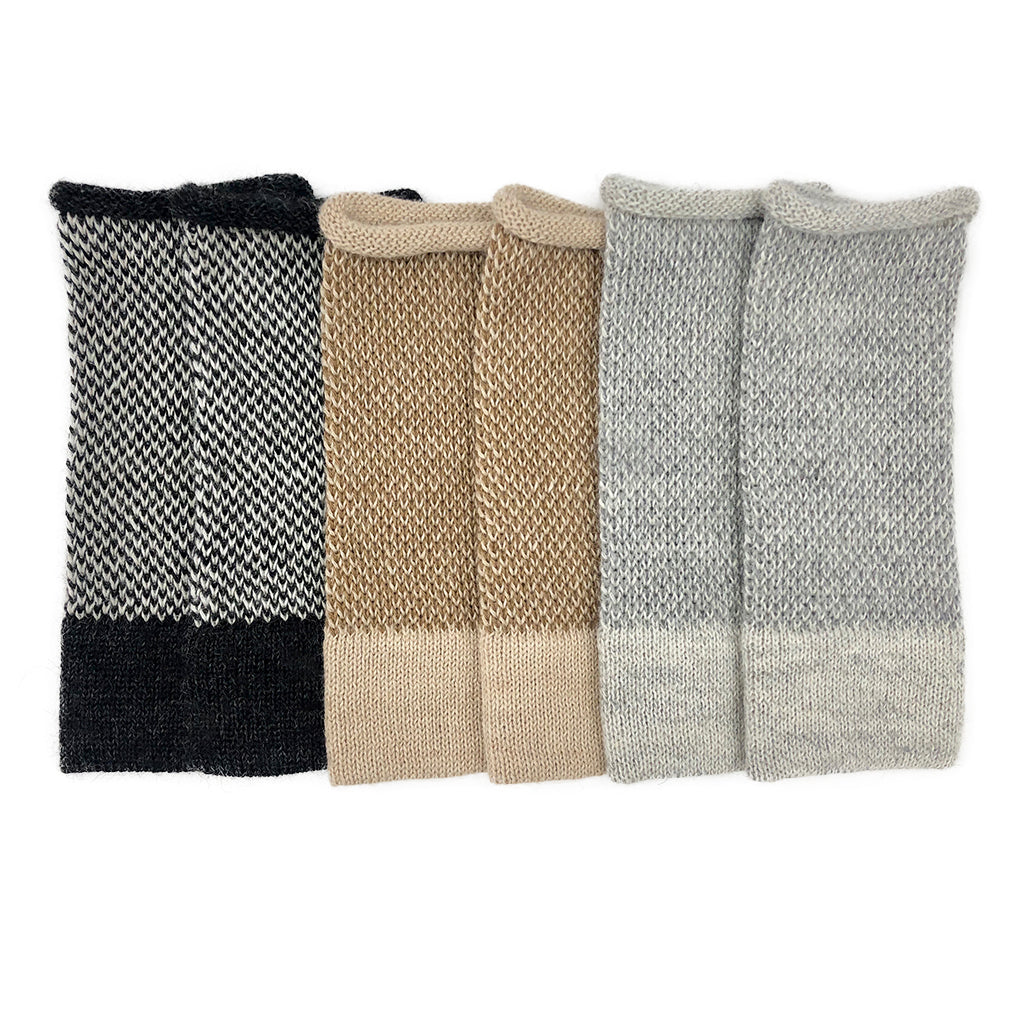 Three pairs of two-tone alpaca fingerless gloves side by side in black and white, camel and gray