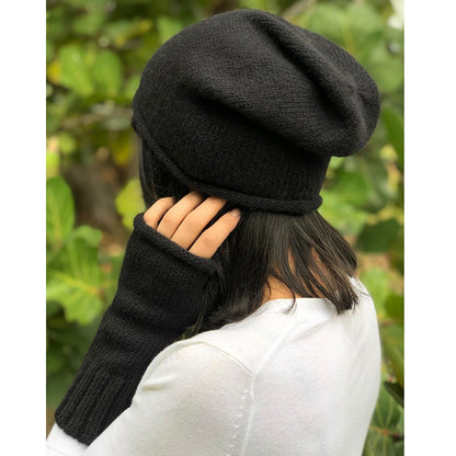 Woman in a white sweater wearing a black slouchy beanie and a black fingerless glove, hand at her ear
