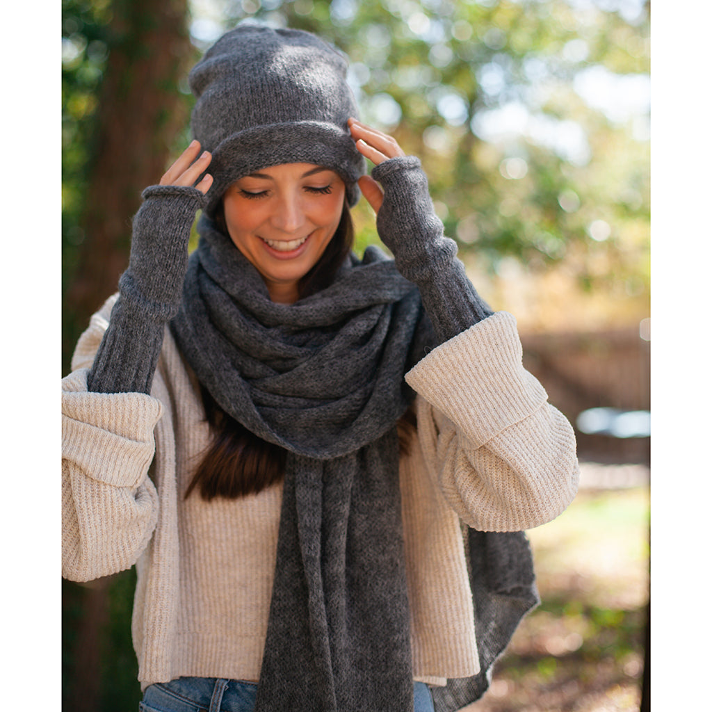 Smiling woman in a charcoal beanie, charcoal fingerless gloves and a long charcoal knit scarf over a cream sweater
