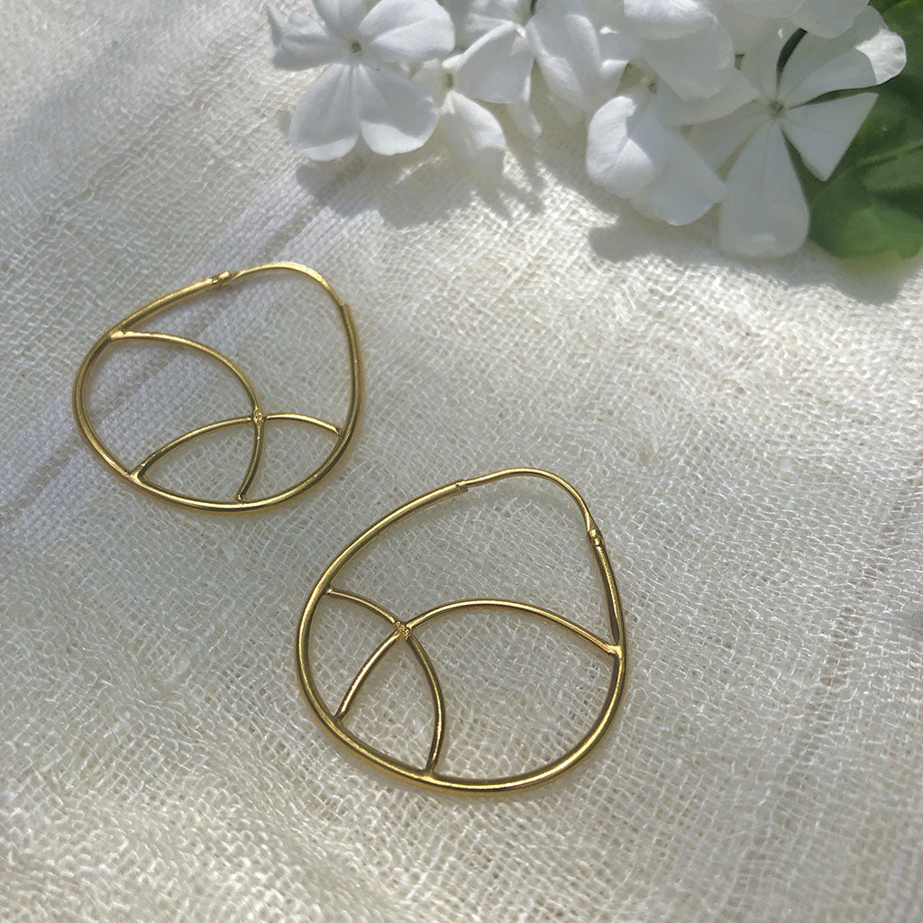 Pair of geometric gold plated hoop earrings on linen beside white flowers