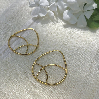Pair of geometric gold plated hoop earrings on linen beside white flowers