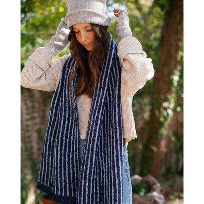Woman in a light gray beanie and gray wrist warmers, hands on the hat, a navy and white striped scarf around her neck