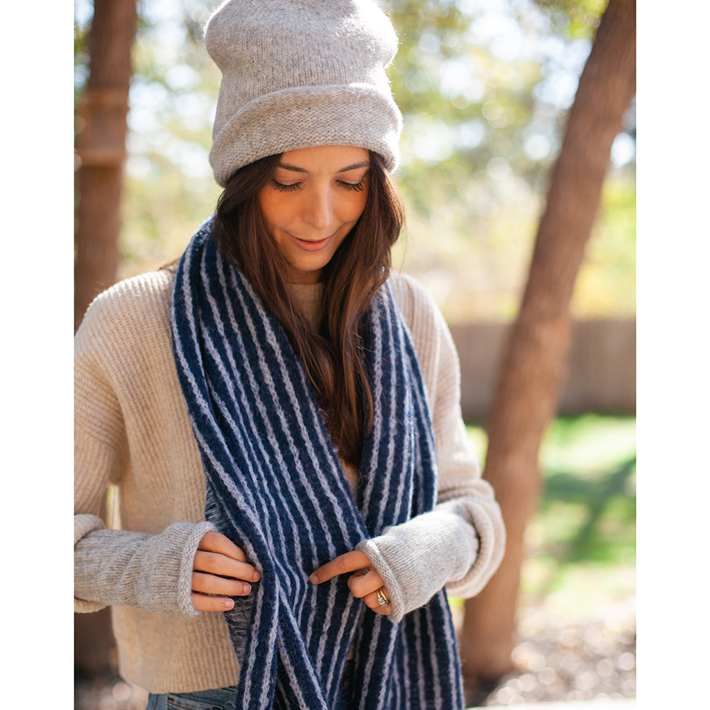 Woman in a cream sweater adjusting a navy and white striped scarf, light gray beanie and gray wrist warmers on