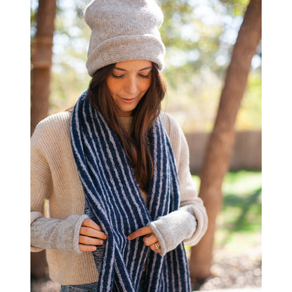 Woman in a cream sweater adjusting a navy and white striped scarf, light gray beanie and gray wrist warmers on