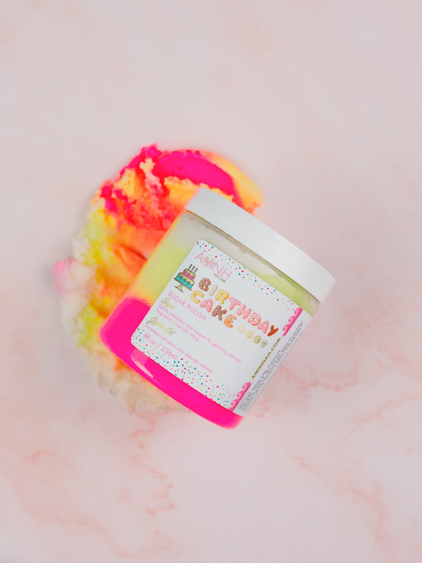 Jar tipped on its side with pink and yellow sugar scrub spilling onto a marble surface.