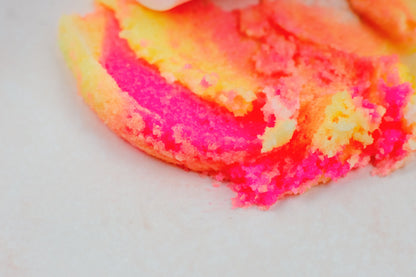 Swirl of pink and yellow sugar scrub smeared across a white surface.