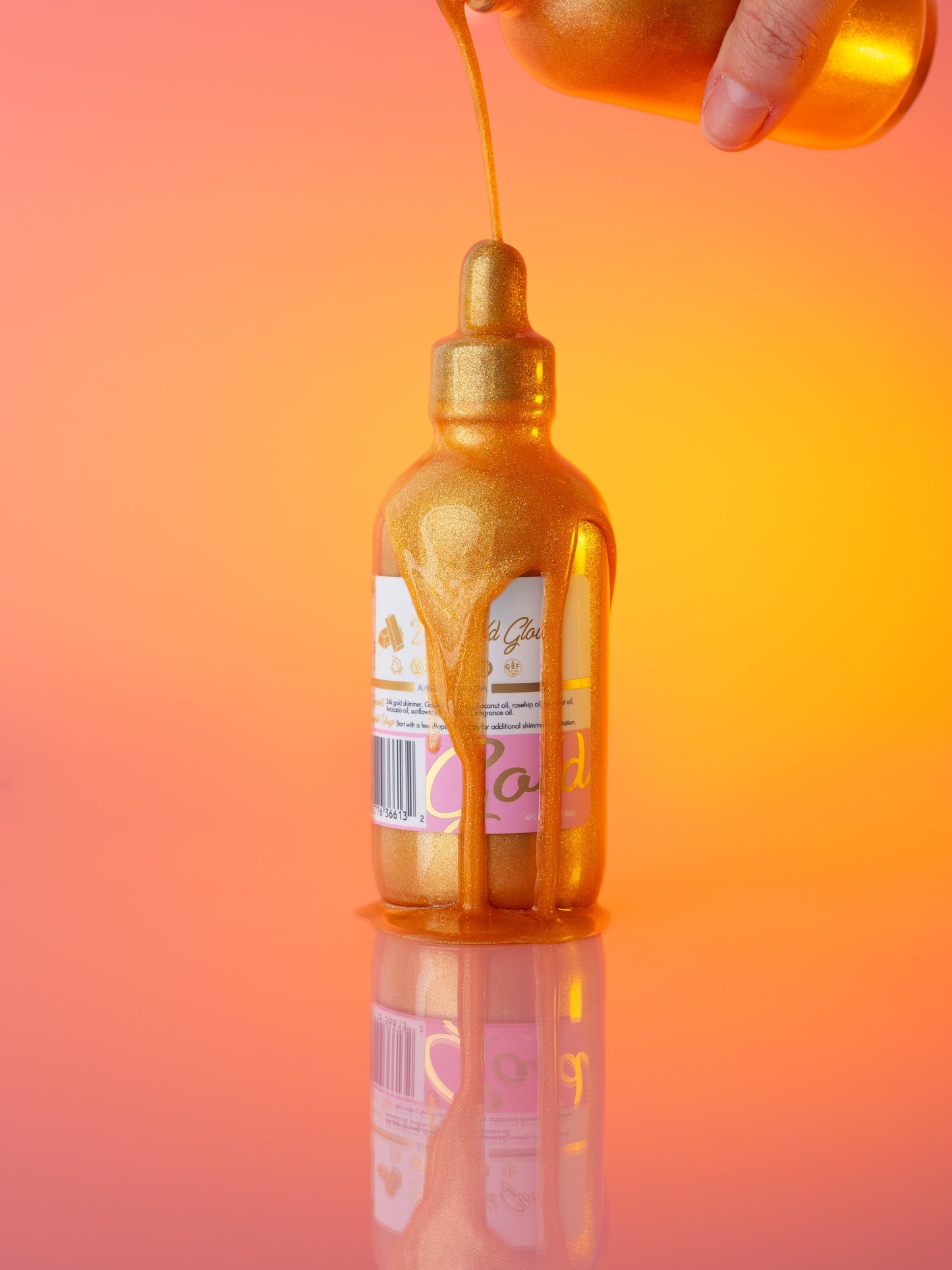 Gold body oil dripping from the pipette back into the bottle, on orange.