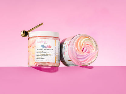 Gold spoon resting on a closed jar beside an open jar showing the pastel swirl, on pink.