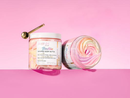 Gold spoon resting on a closed jar beside an open jar showing the pastel swirl, on pink.