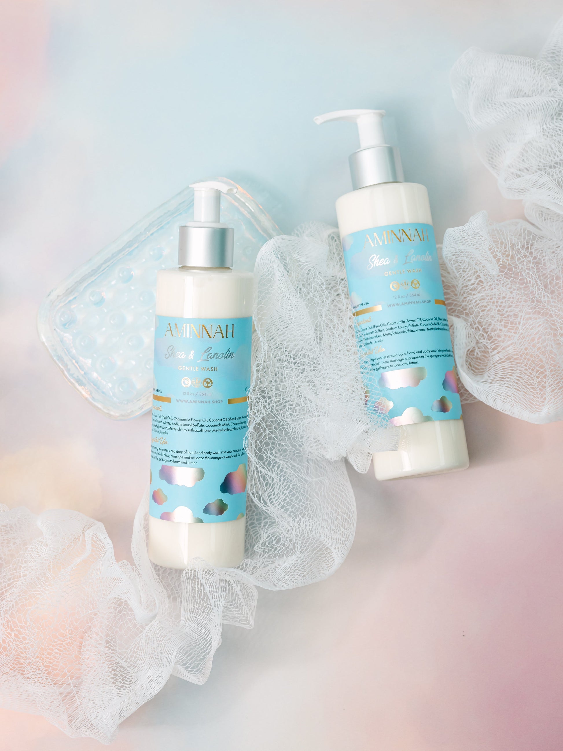 Two cleanser bottles with a mesh bath puff on a pastel background.