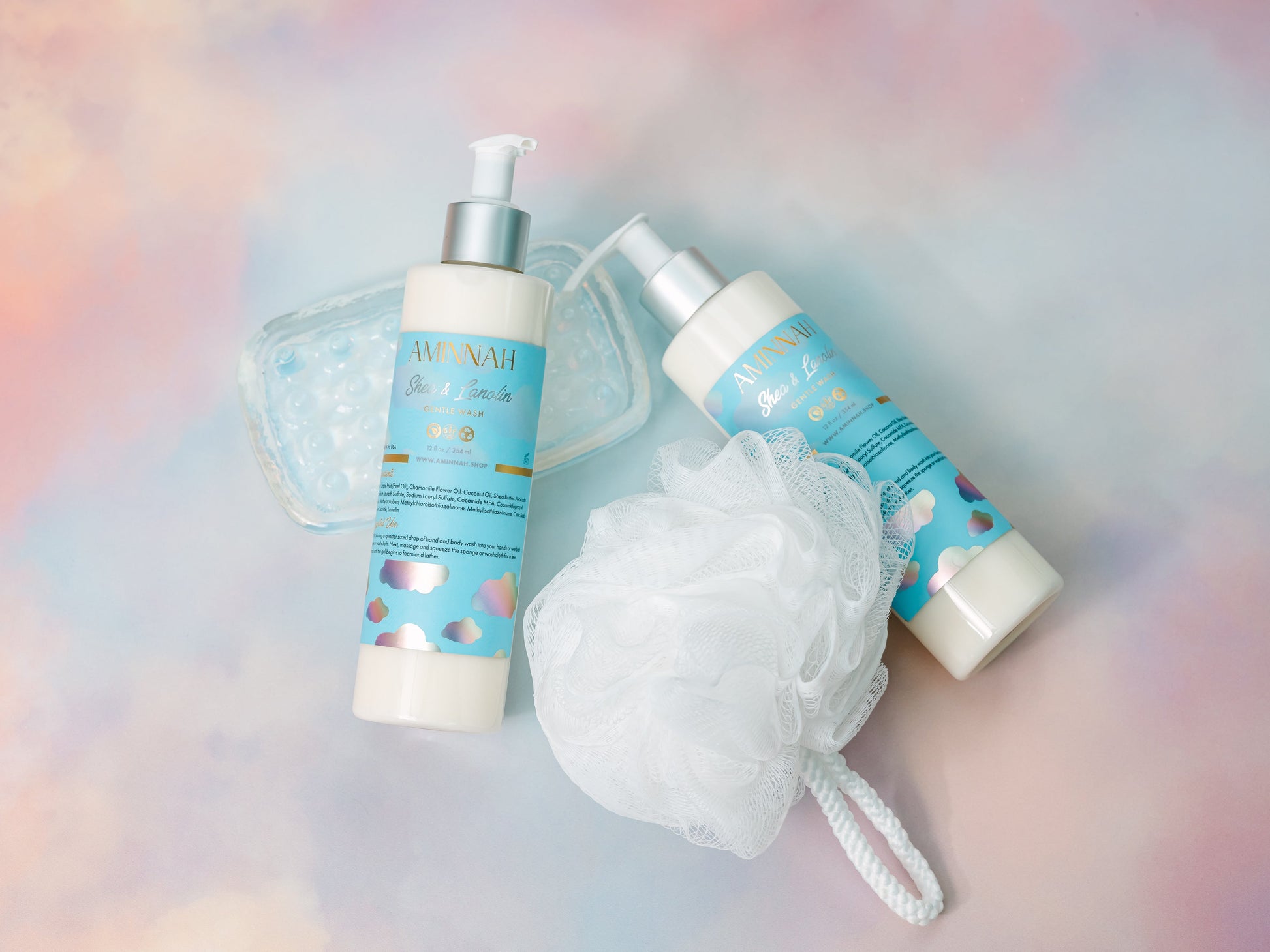 Cleanser bottles beside a white mesh bath puff on pastel.