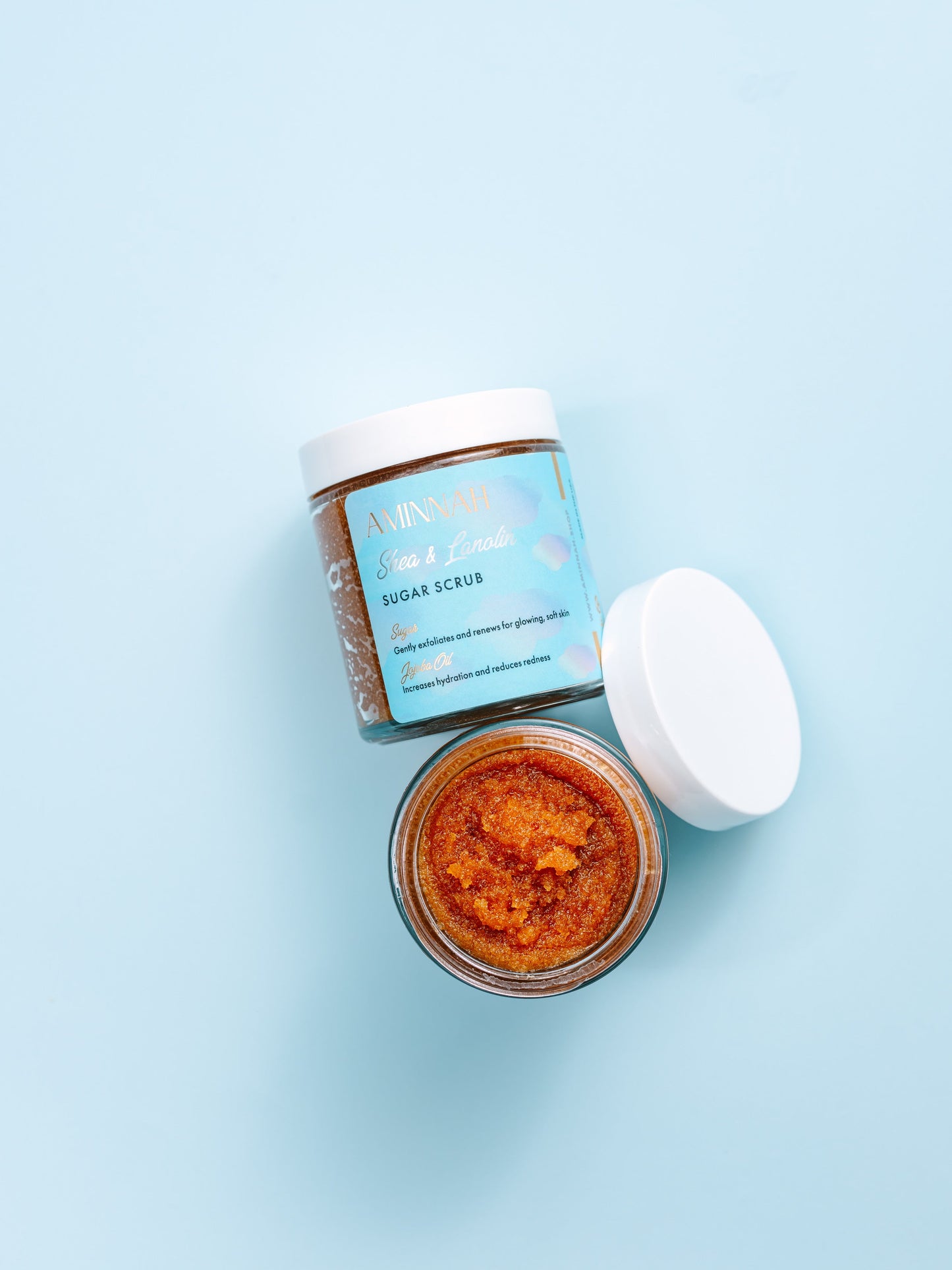 Open jar of brown sugar scrub with the lid resting beside it on a blue background.