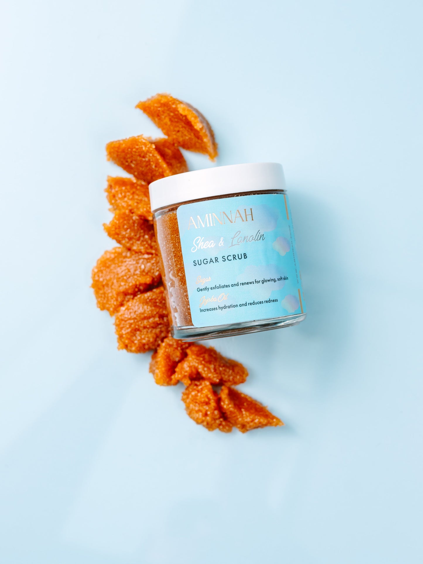 Jar with brown sugar scrub spilling out in a swirl on blue.