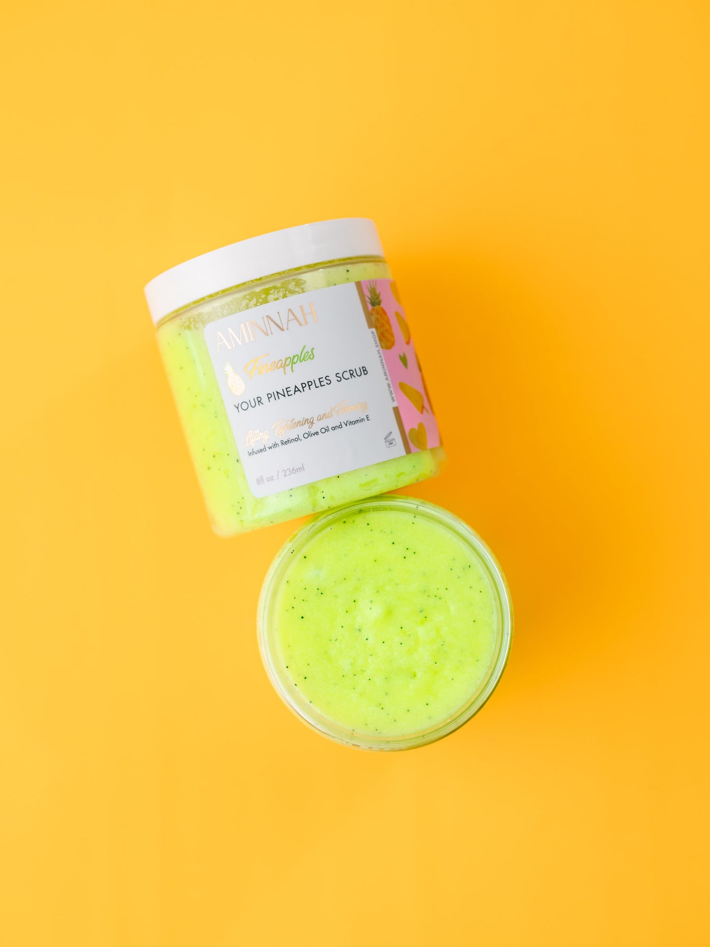 Open jar of green sugar scrub with the lid propped beside it on yellow.