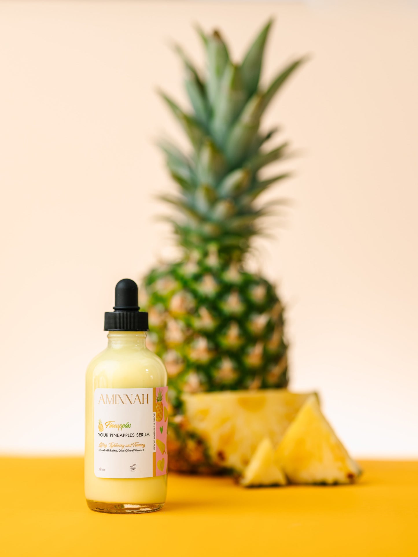 Serum bottle standing in front of a whole pineapple on yellow.