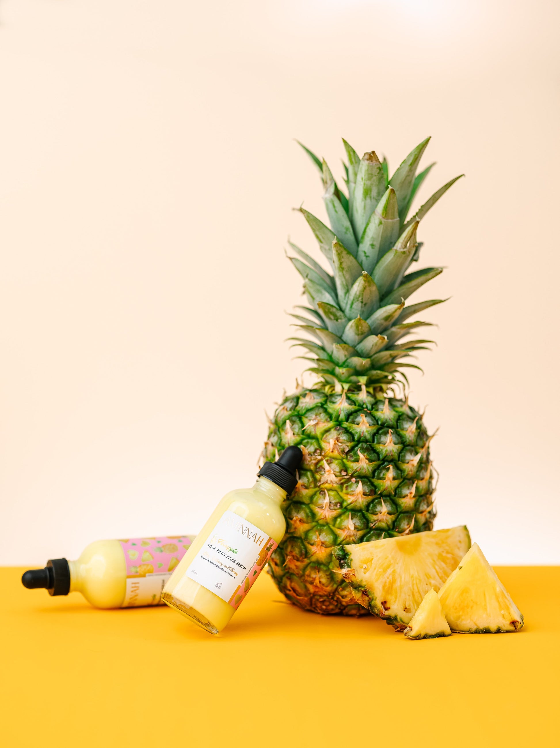 Serum bottle and jar arranged in front of a whole pineapple.
