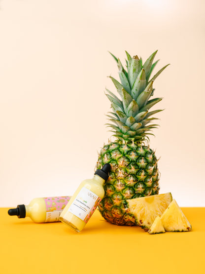 Serum bottle and jar arranged in front of a whole pineapple.