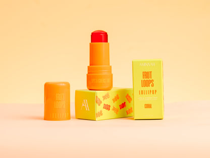 Coral lip and cheek tint standing beside its yellow carton on peach.