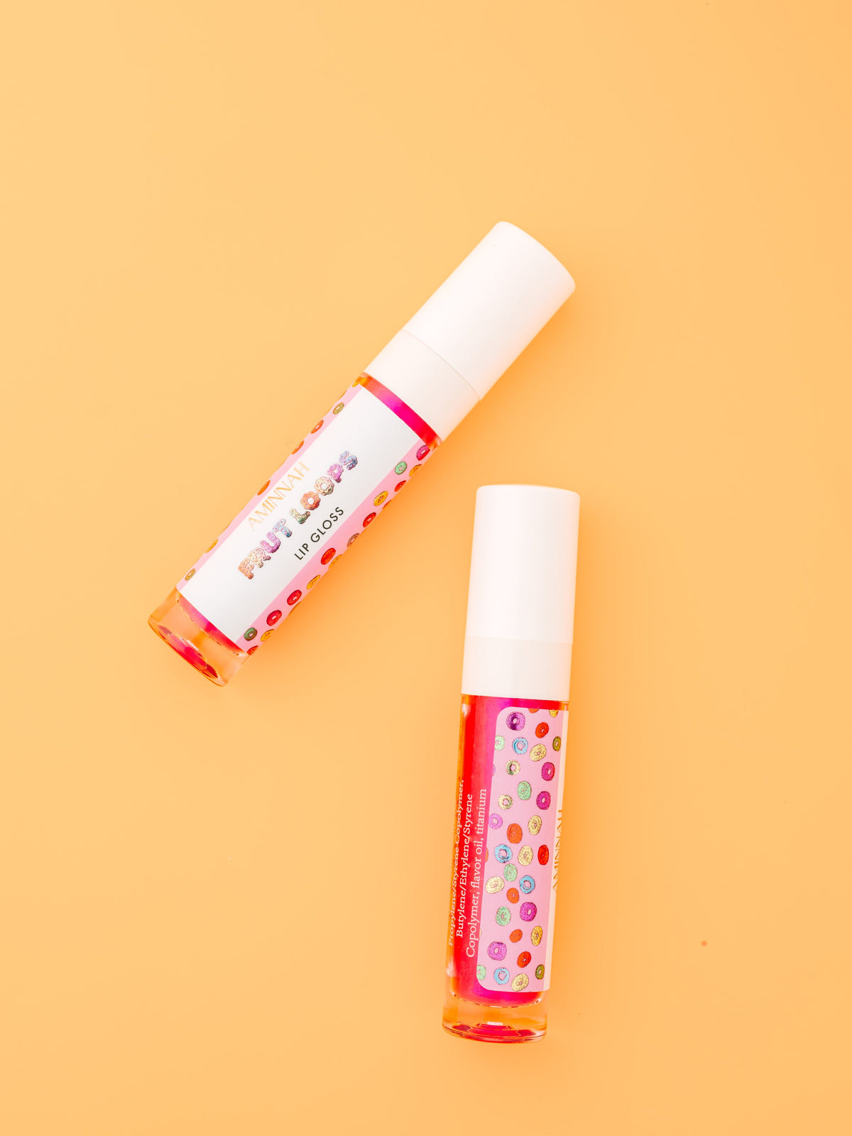 Two lip gloss tubes lying side by side on an orange background.