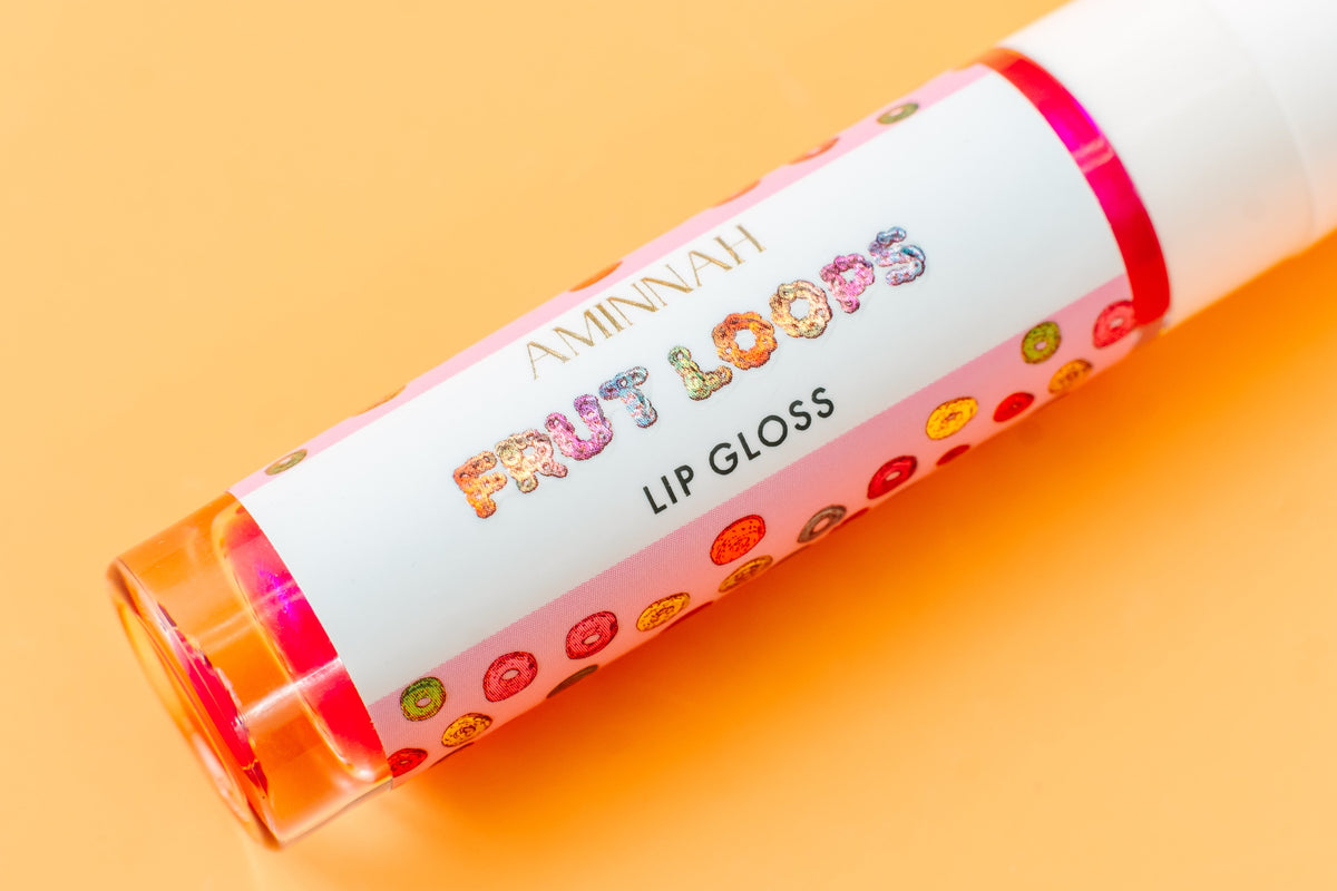 Lip gloss tube lying on orange with the Frut Loops label facing up.