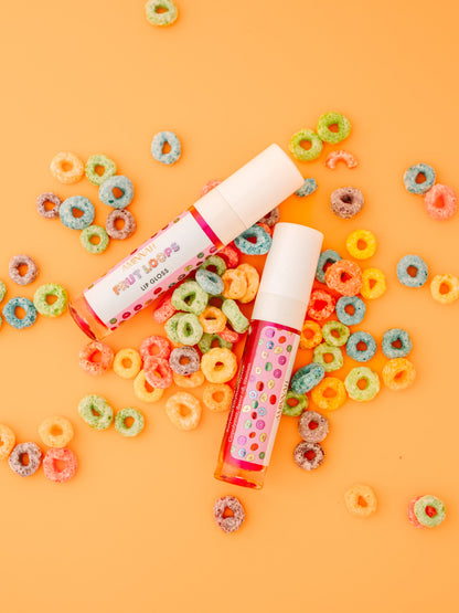Two lip gloss tubes on a scatter of coloured cereal loops.
