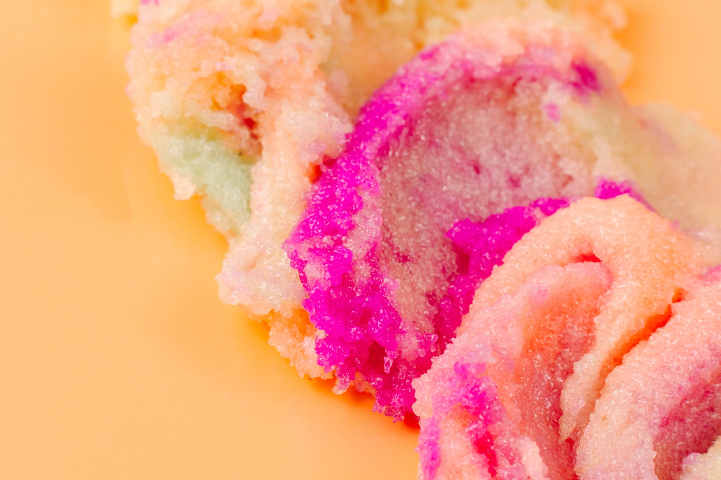 Pink and cream sugar scrub texture spread across a peach background.