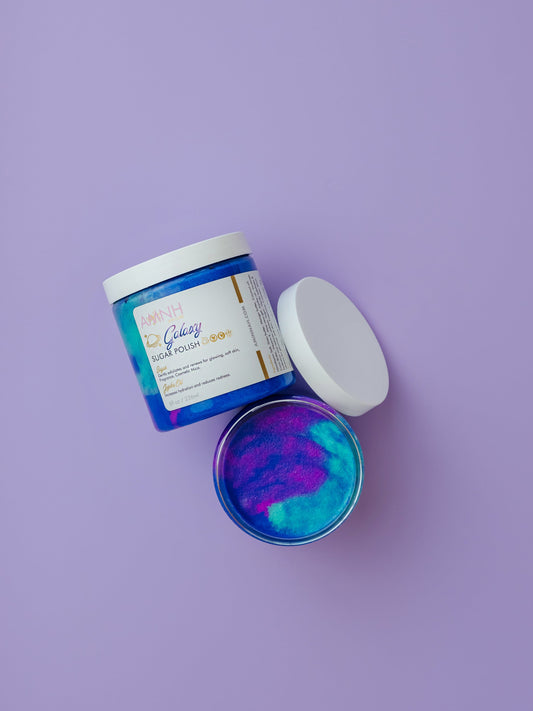 Jar of galaxy scrub with the lid propped beside it on purple.