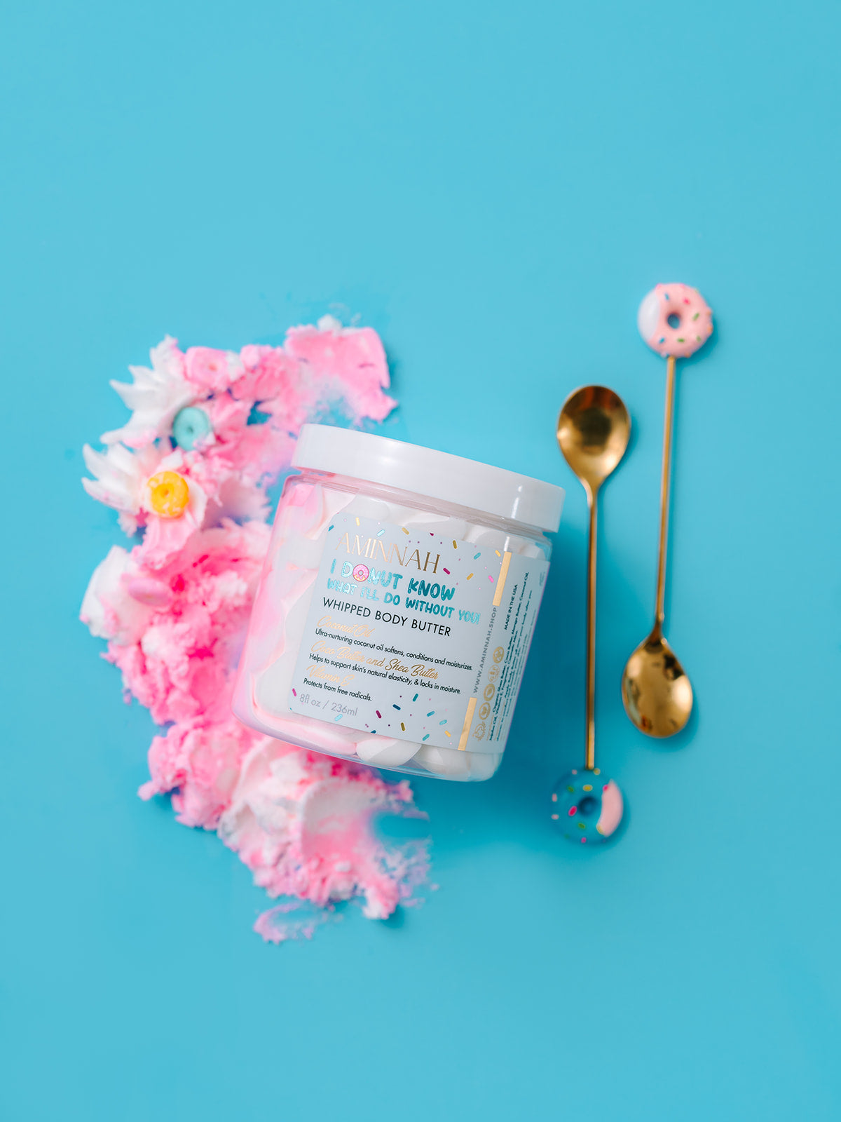 Open jar of pink whipped butter with a gold spoon beside it on blue.