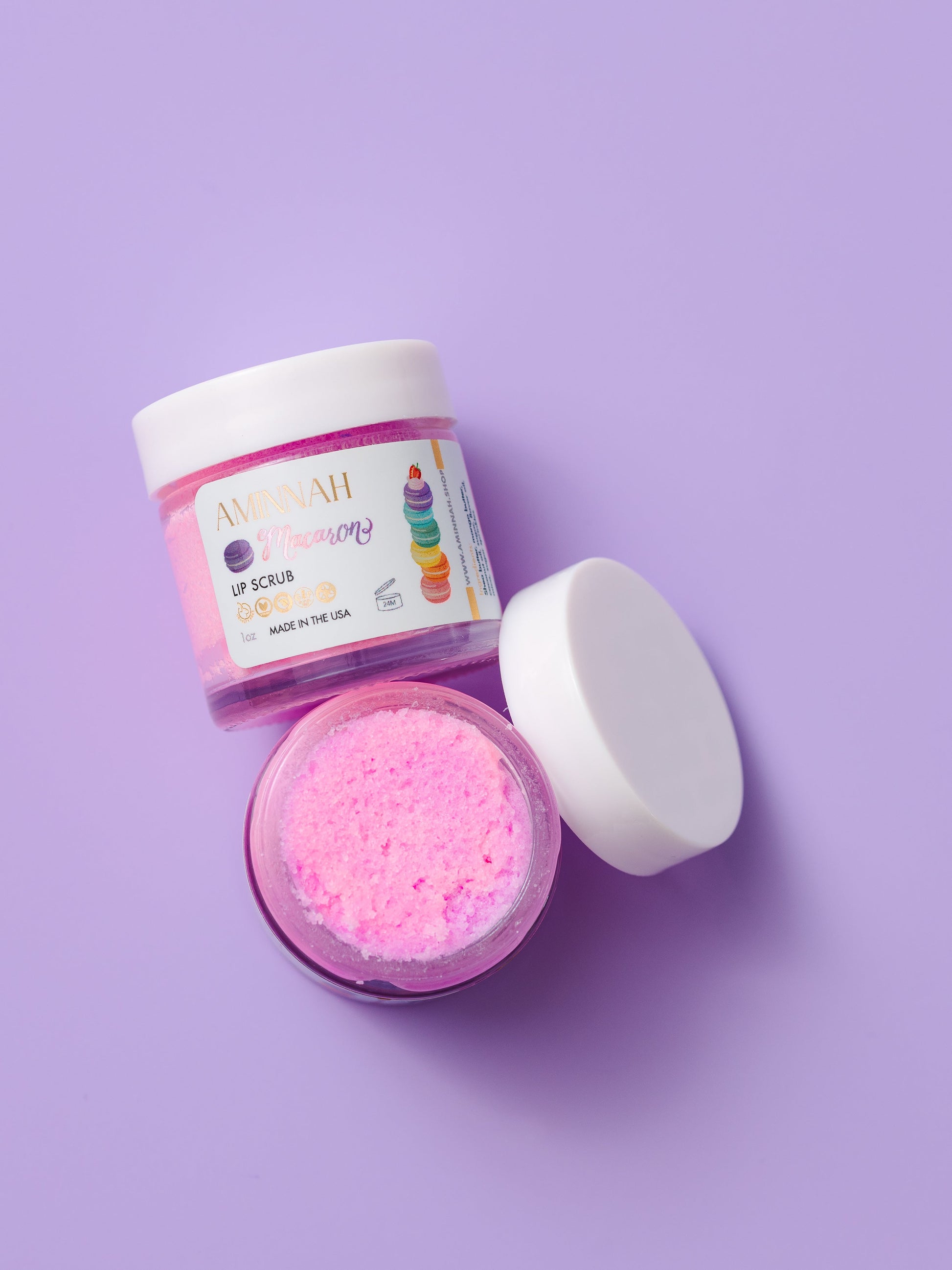 Open jar of pink lip scrub with the lid beside it on purple.