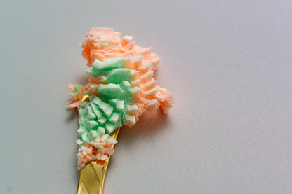 Ribbon of green and orange whipped butter across a grey background.