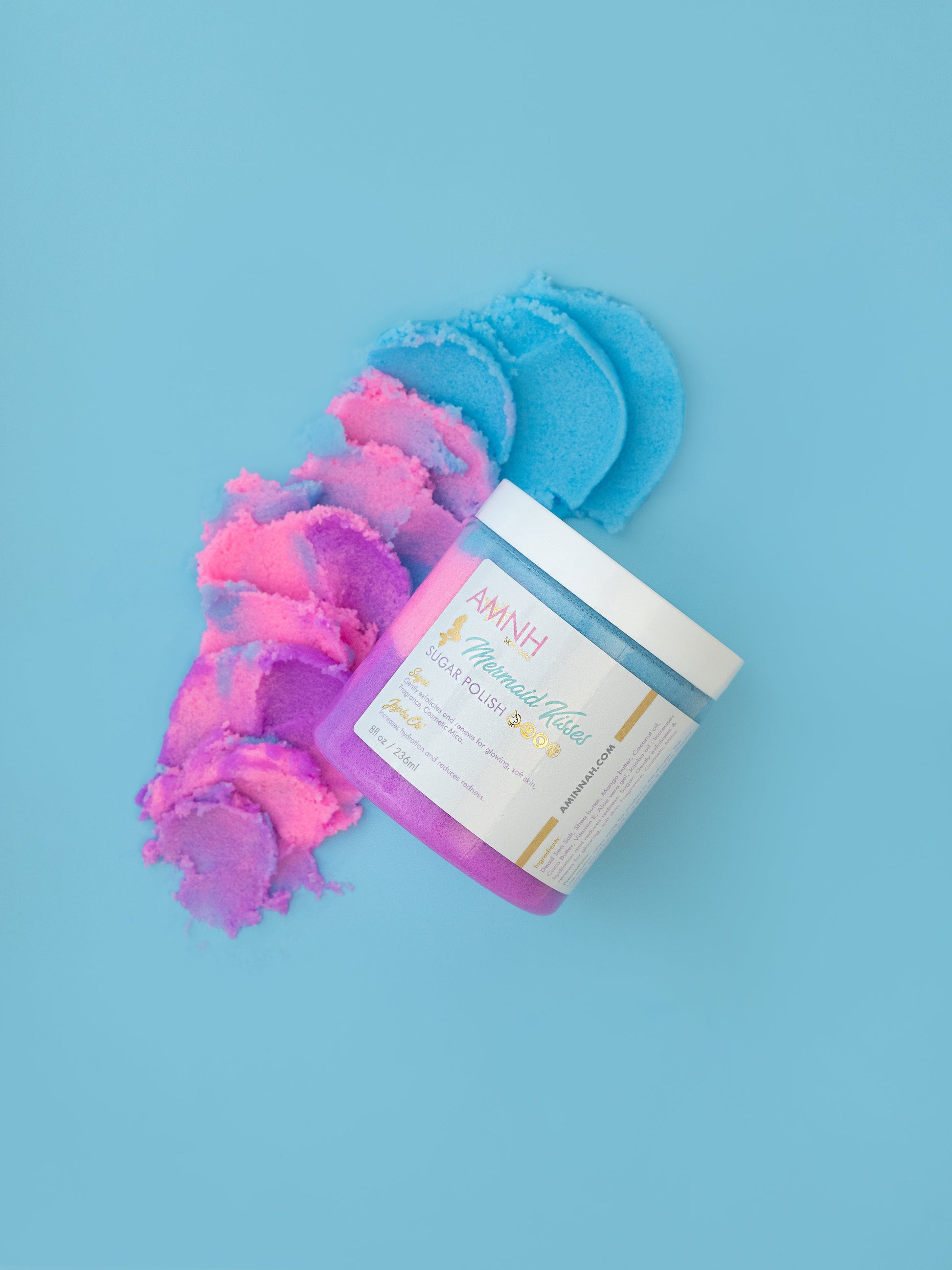 Jar with pink and blue sugar scrub spilling out on a blue background.