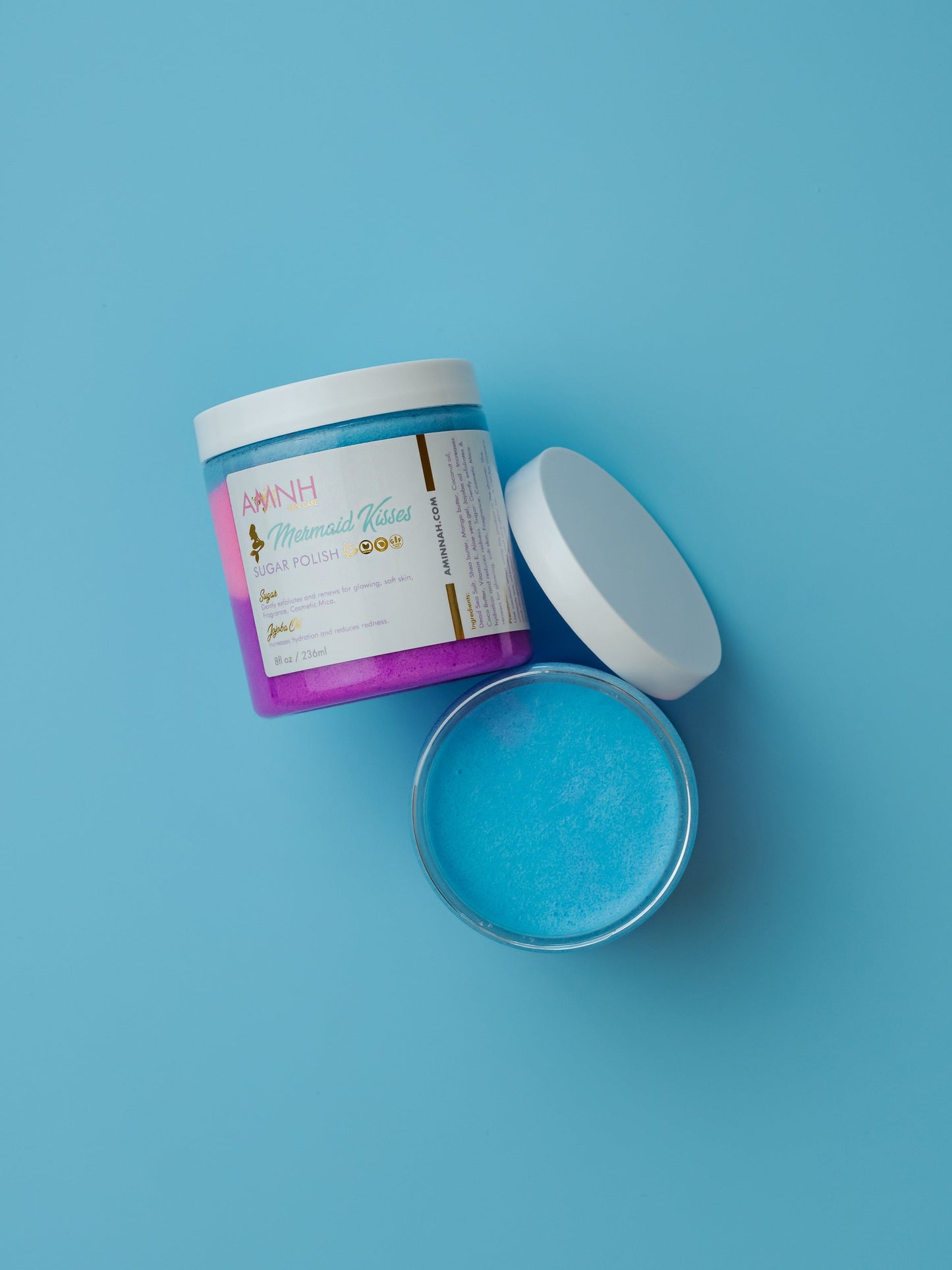 Jar of scrub with the lid propped beside it on blue.