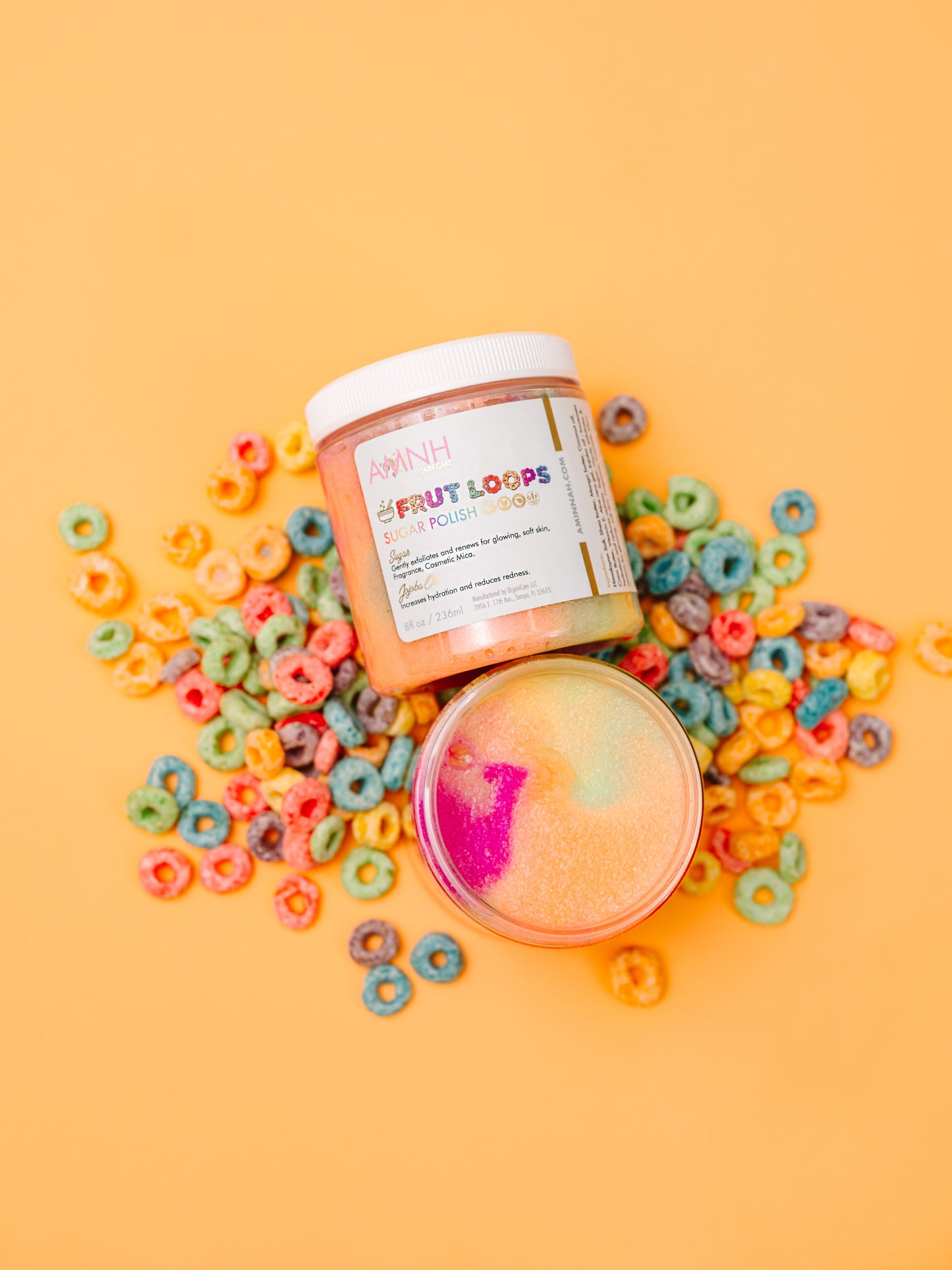 Jar of scrub with cereal loops and sprinkles scattered around it on orange.