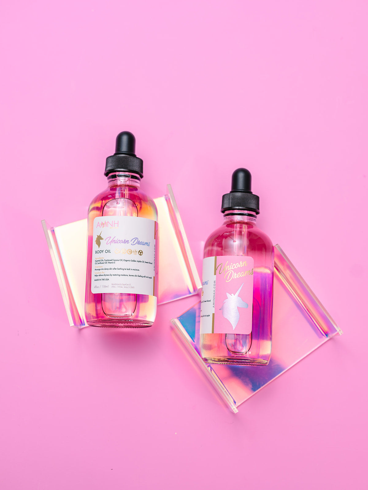Two body oil bottles beside an iridescent prism on pink.