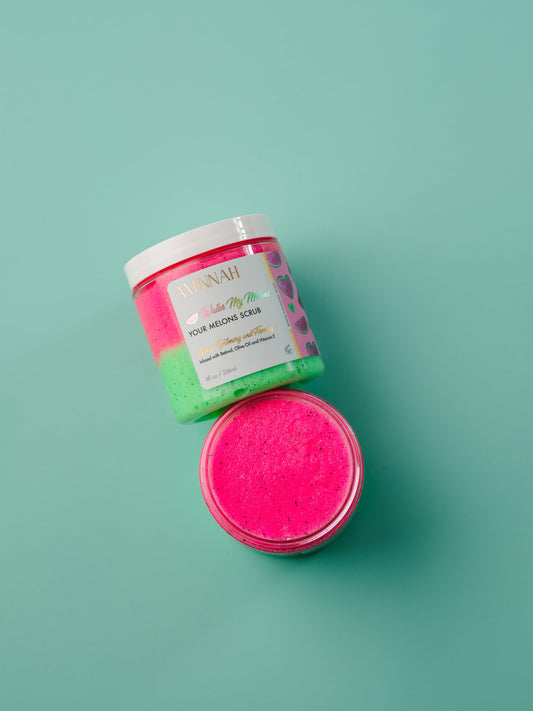 Open jar of pink sugar scrub with the lid beside it on mint.