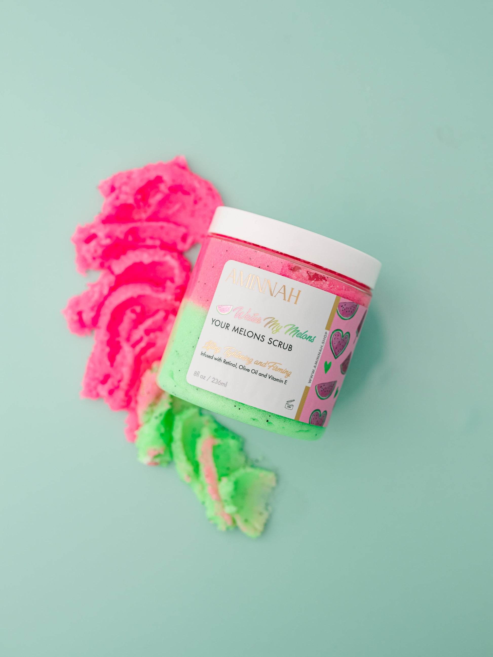 Jar with a pink scrub swirl piled beside it on mint.