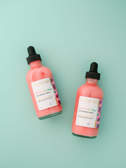 Two pink serum bottles with black dropper caps on mint.