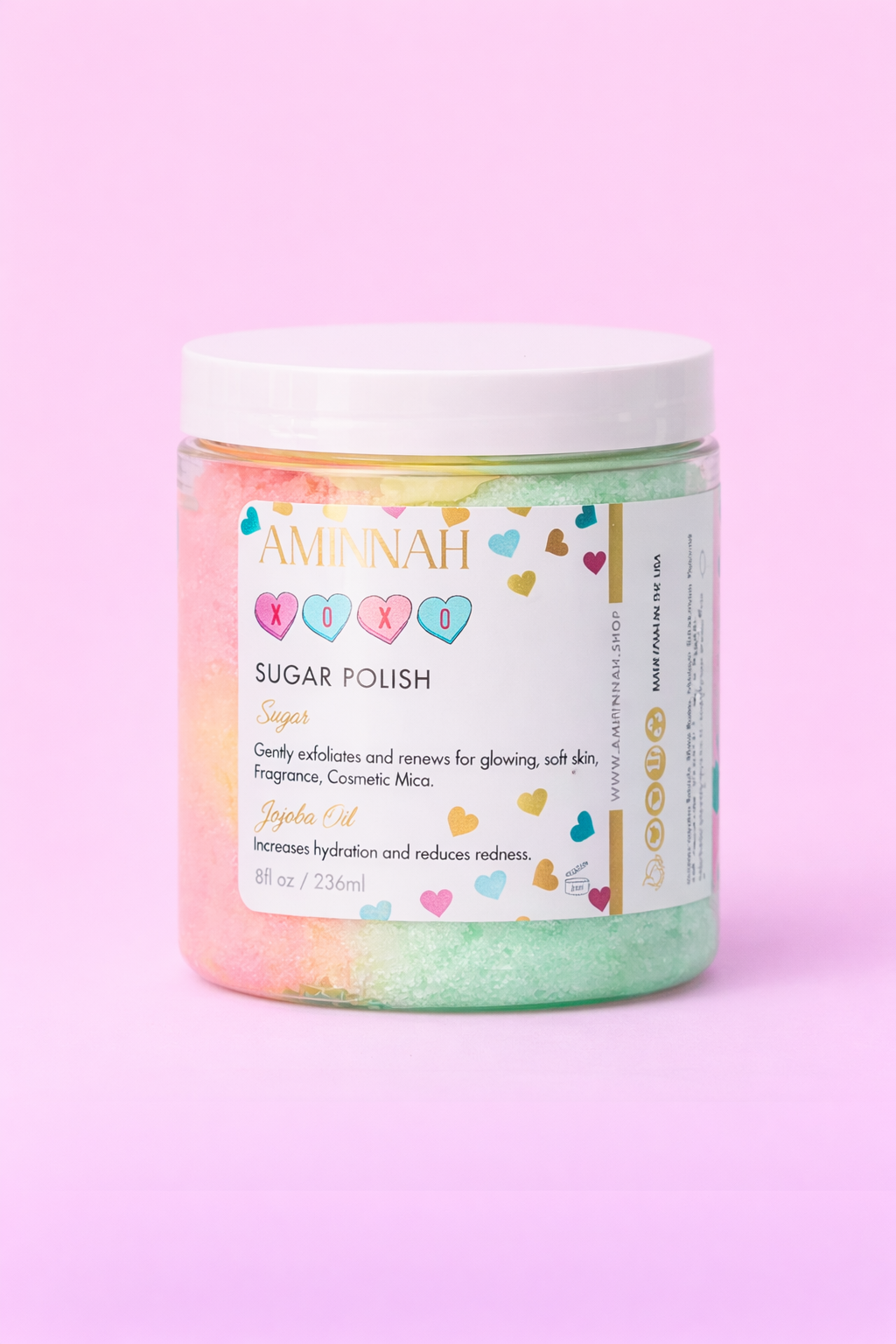 Jar of XOXO sugar scrub with the colourful label facing forward on pale pink.
