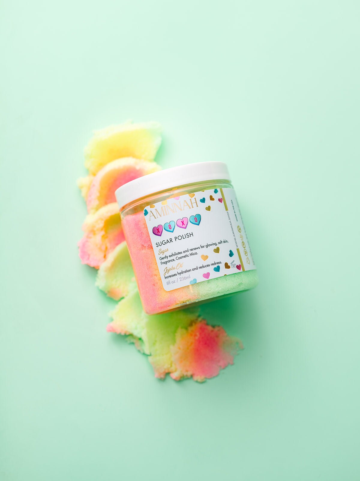 Jar with yellow and pink sugar scrub piled on top, on mint.