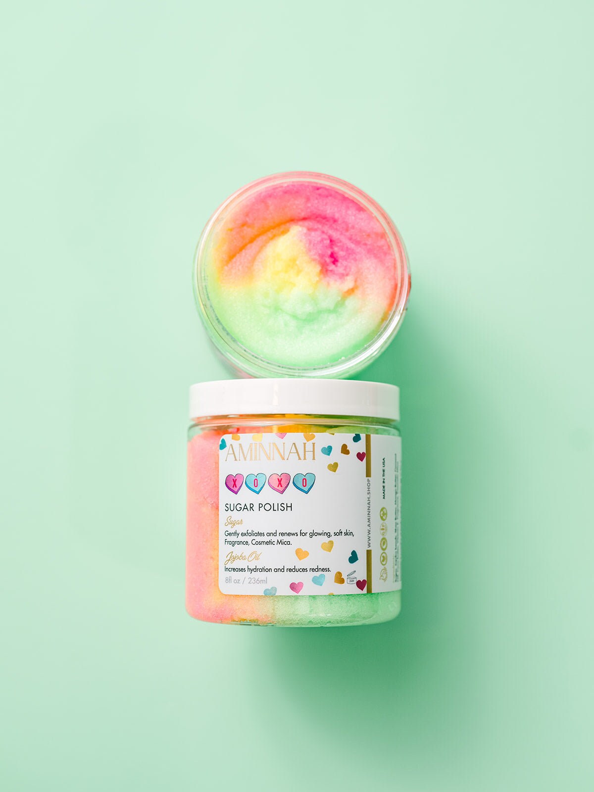 Jar with a pastel scrub swirl and the lid beside it on mint.