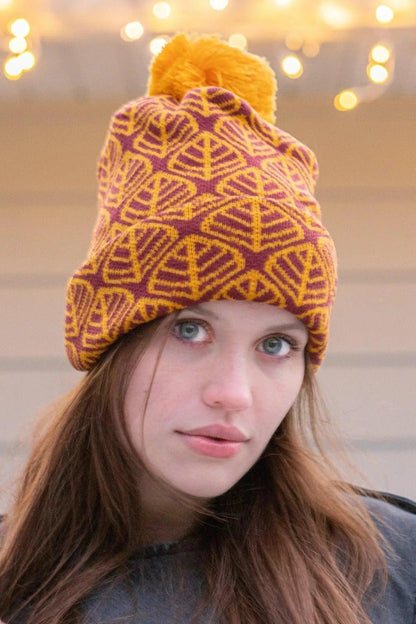 Model wearing the burgundy and gold leaf beanie under string lights